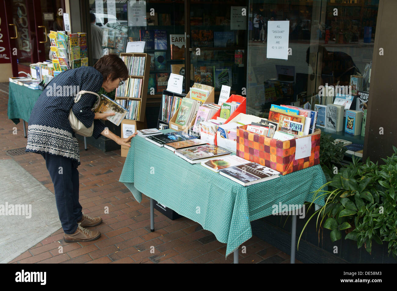 Frau mittleren Alters Surfen an Bücher über einen Verkauf Tisch draußen eine unabhängige Buchhandlung, Vancouver, BC, Kanada Stockfoto