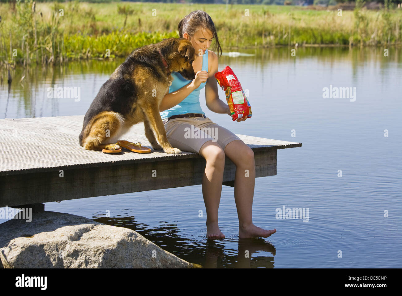 Junges Mädchen und ihr Hund Essen Kartoffelchips außerhalb an einem See Stockfoto