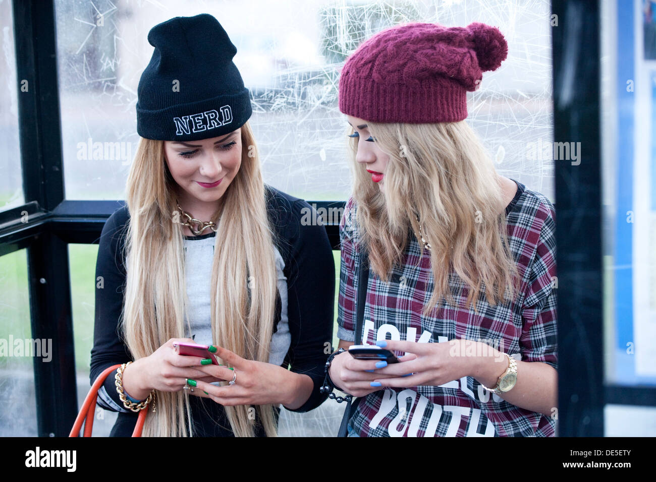Zwei Mädchen im Teenageralter sitzen im Bus Stop mobil telefonieren. Stockfoto