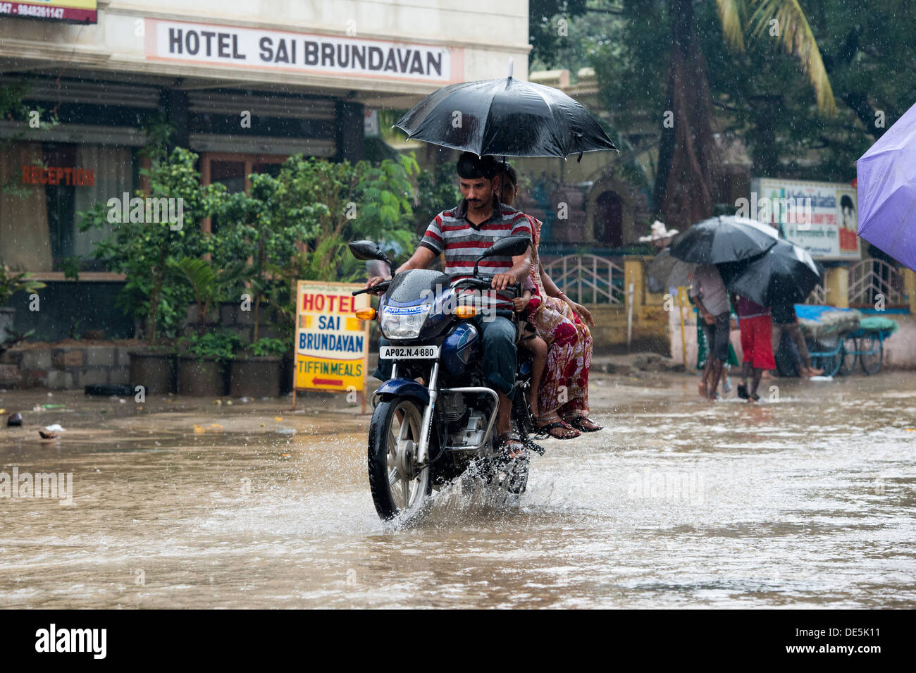 Indische Familie auf einem Motorrad mit Regenschirm Reiten durch nassen überfluteten Straßen in Puttaparthi, Andhra Pradesh, Indien Stockfoto