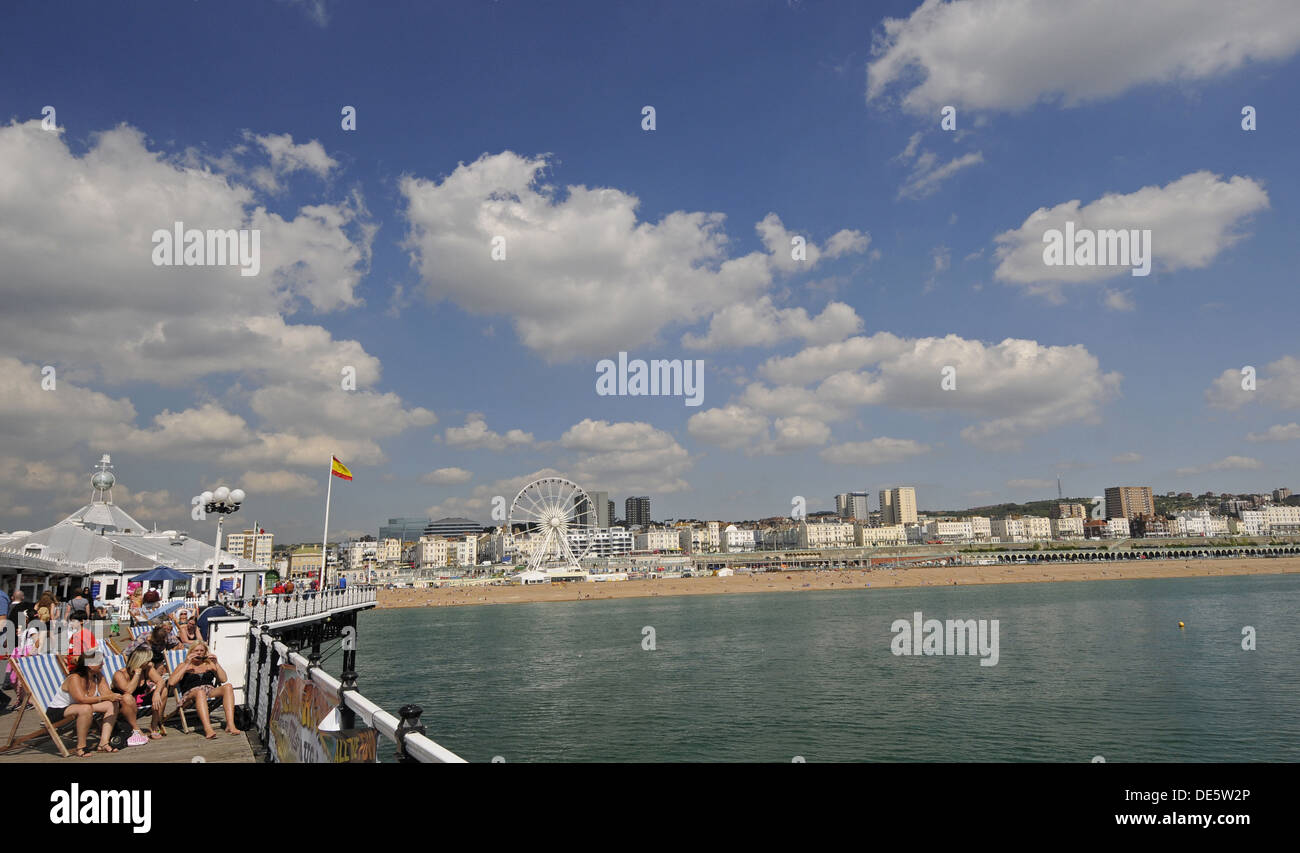 Touristen, die zum Sonnenbaden auf der Brighton Pier mit Strand im Hintergrund East Sussex England Stockfoto