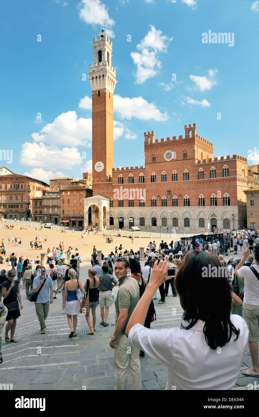 Touristen auf der Piazza del Campo, dem zentralen Platz der Stadt Siena, Toskana, Italien. Torre del Mangia Turm erhebt sich hinter Stockfoto