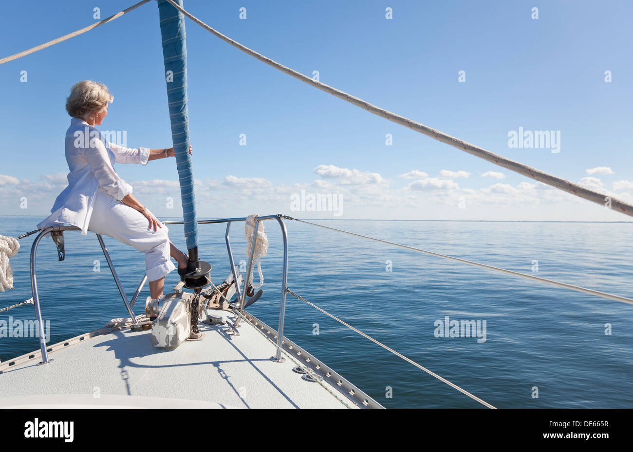 Eine glückliche senior Frau sitzen am Bug eines Segelbootes mit Blick auf das ruhige blaue Meer Stockfoto