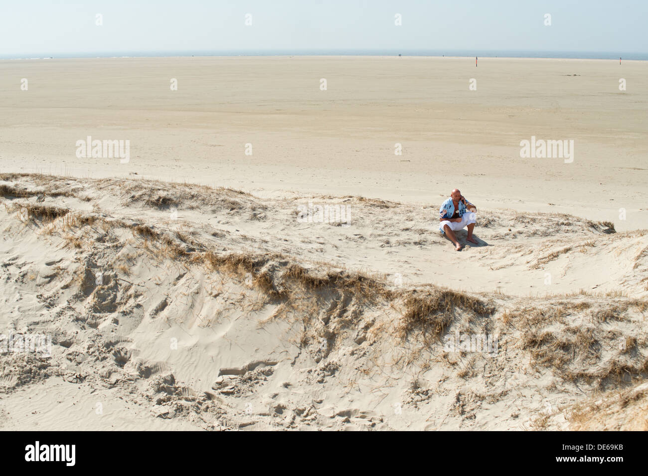 Sankt Peter-Ording, Deutschland, ein Mann sitzt im Sand und Telefon Stockfoto