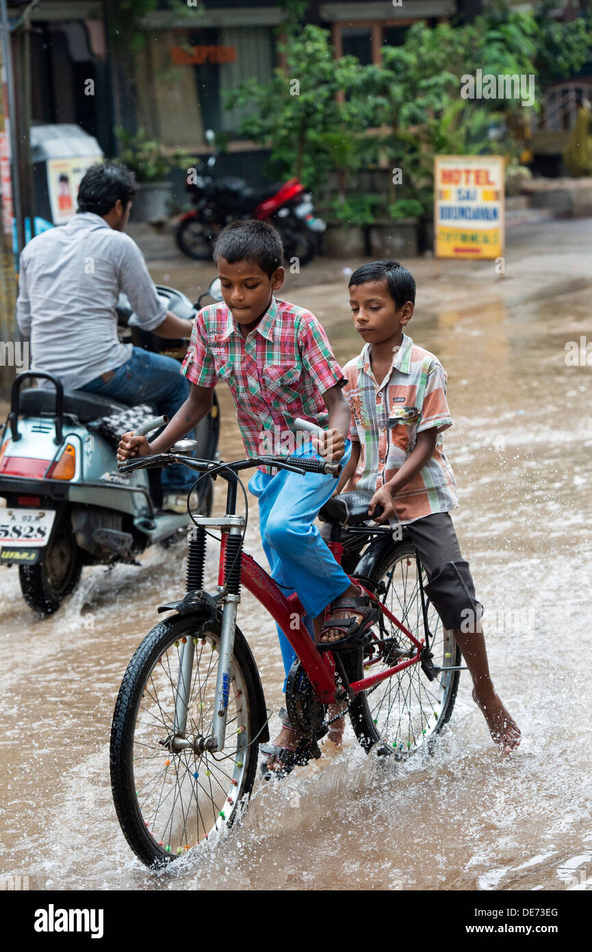 Indianerdorf jungen durchlaufen einer überfluteten Straße während des Monsuns. Puttaparthi, Andhra Pradesh, Indien Stockfoto