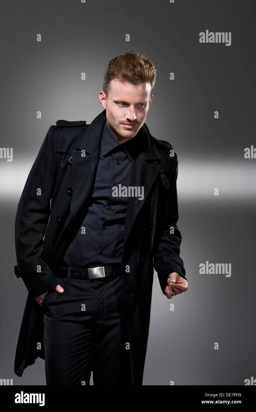 Mitte erwachsener Mann im schwarzen Mantel stehen vor grauem Hintergrund Stockfoto
