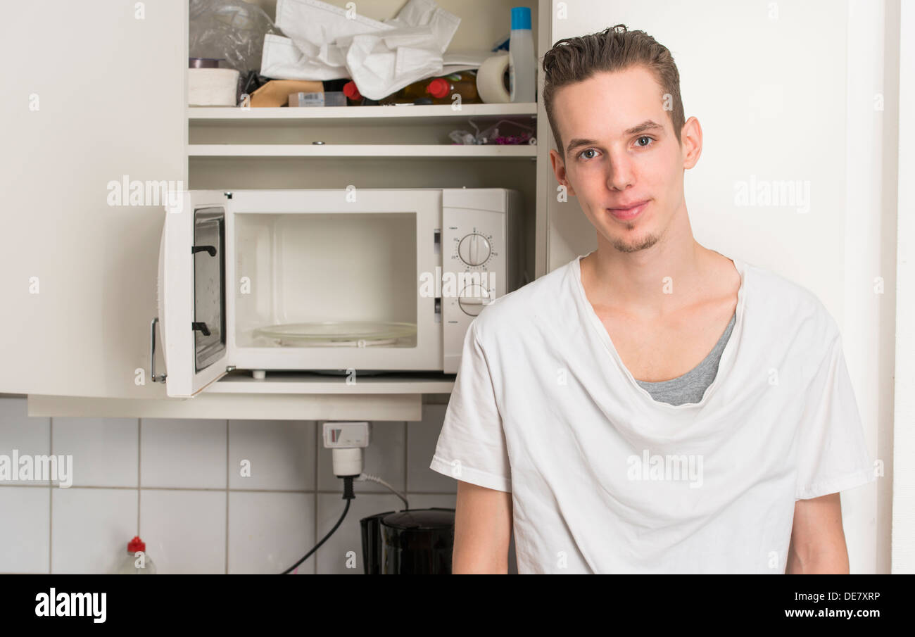 Junger Mann stehend in einem chaotischen Küche mit offener Mikrowelle Stockfoto