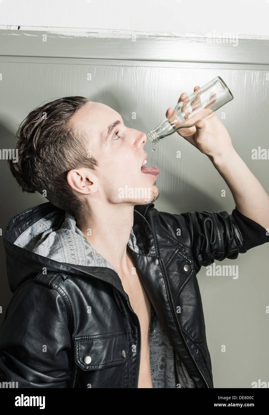 Profil-Porträt eines jungen Mannes, den letzten Tropfen aus einer leeren Flasche trinken Stockfoto