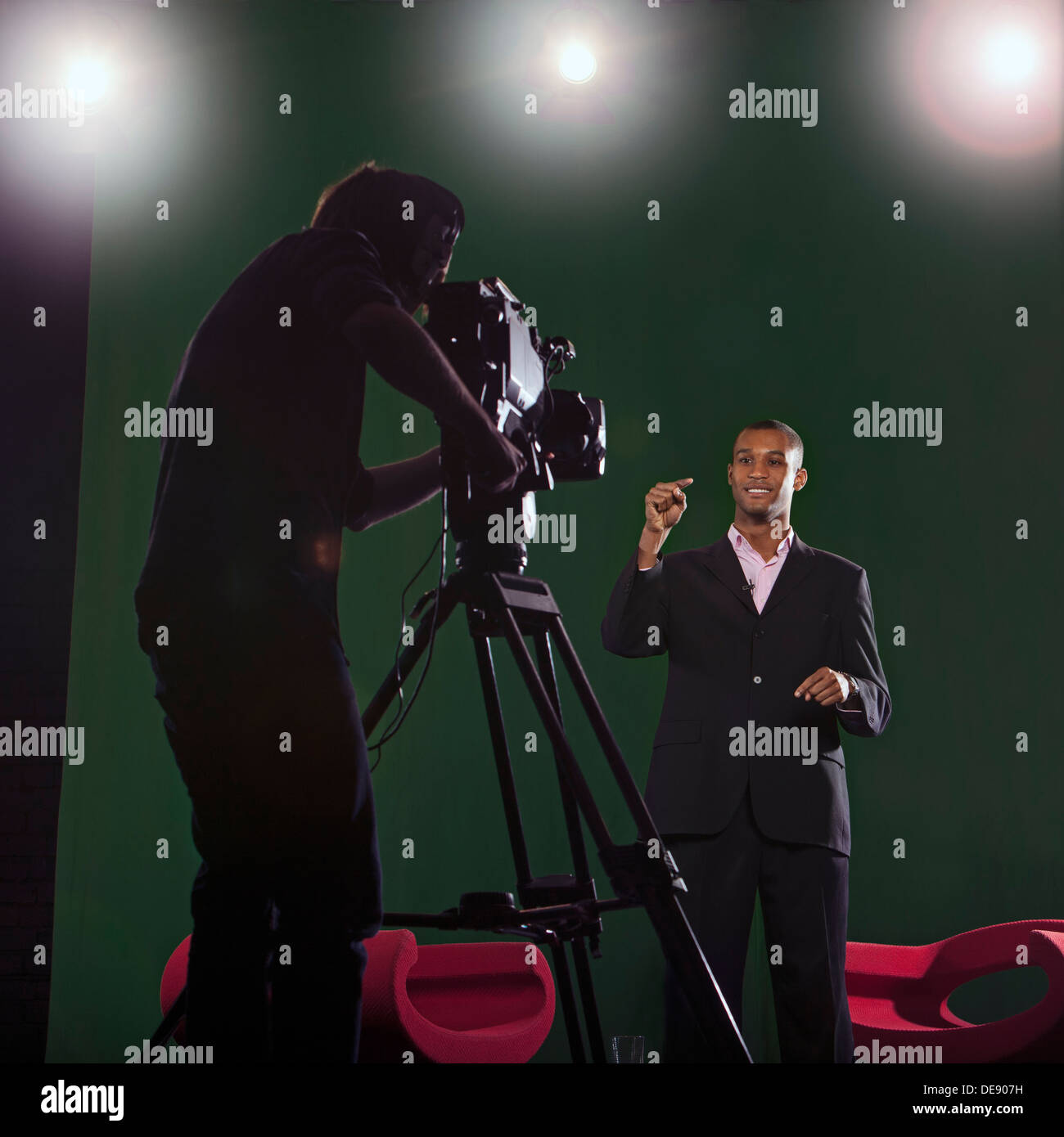 Moderator im Gespräch mit Kamera mit Silhouette der Kameramann im Vordergrund und Studio Lichter im Hintergrund. Stockfoto