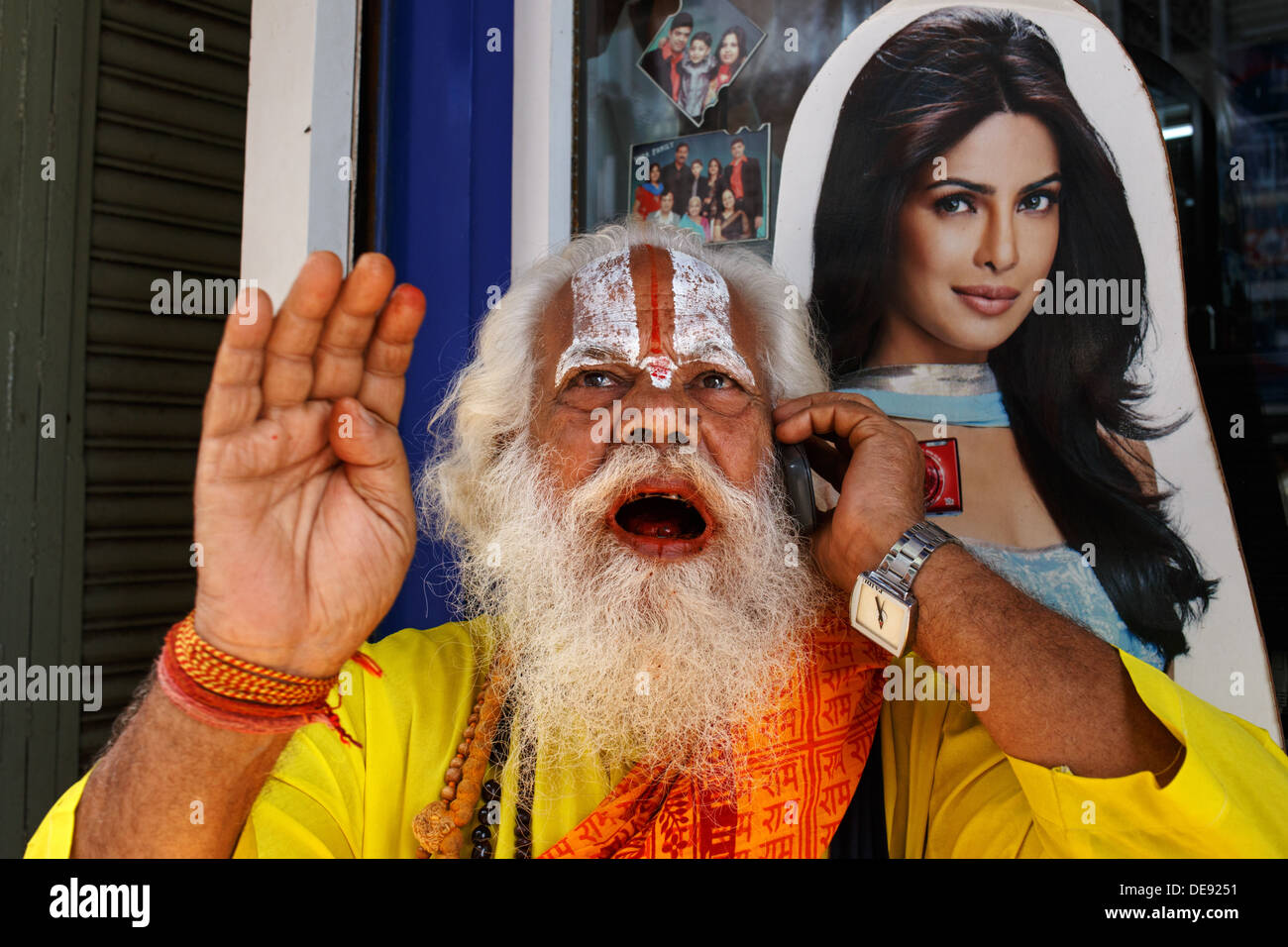 Ein Hindupriester spricht über ein Mobiltelefon (Handy) in zentralen Mumbai, Indien mit einem Plakat Werbung für Digitalkameras hinter Hallo Stockfoto