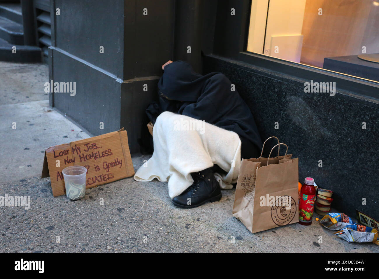 Eine obdachlose Person drängte sich auf einem Bürgersteig vor einem Laden in eine Decke. Stockfoto