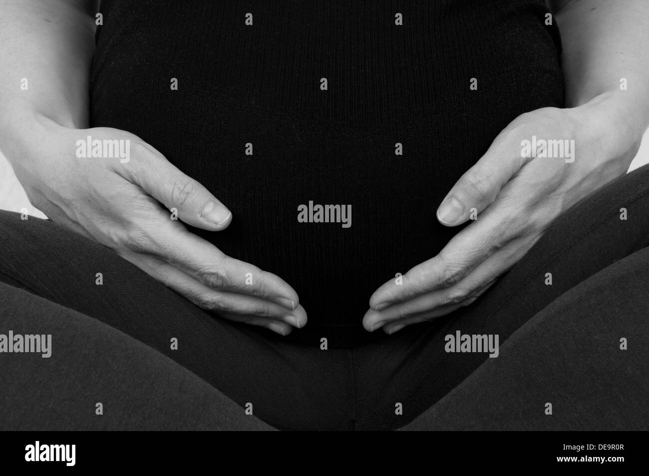 Schwarz / weiß beschnitten Schuss einer schwangeren Frau mit ihren Händen um ihr ungeborenes Baby-Bauch Stockfoto
