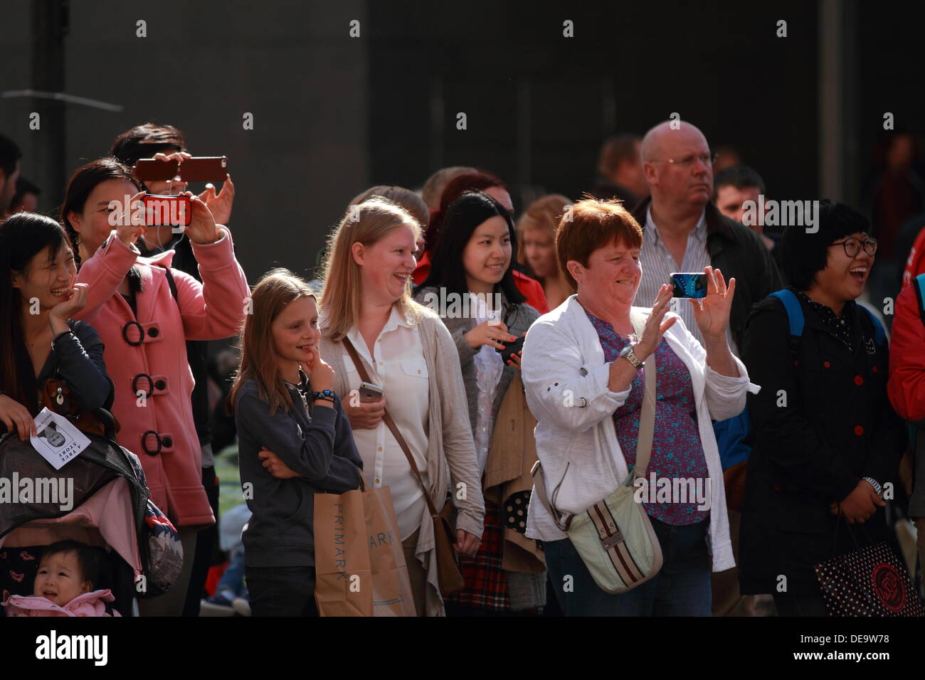 Eine Gruppe von Männern, Frauen und Kinder, die eine Leistung und aufnehmen von Bildern auf dem Handy anzeigen. Einem sonnigen Tag draußen, Glasgow, Scotland, UK Stockfoto