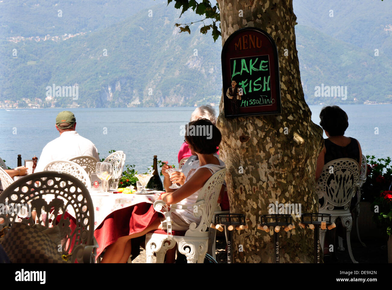 Italien - Comer See - Varenna - Baum schattigen Restaurant über dem blauen See-Wasser - Kunden an Tischen - Sonnenlicht und Schatten Stockfoto