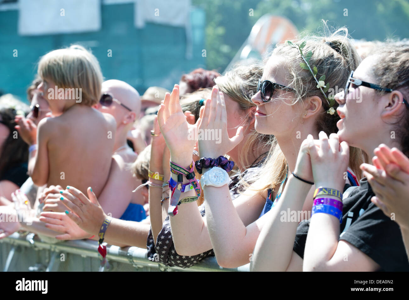 Glückliche hübsche weiße Teenager-Mädchen mit Blumen in den Haaren, Armreifen an ihren Handgelenken an der Vorderseite einer Barriere auf einem Sommer-Musikfestival Pre-Covid Stockfoto