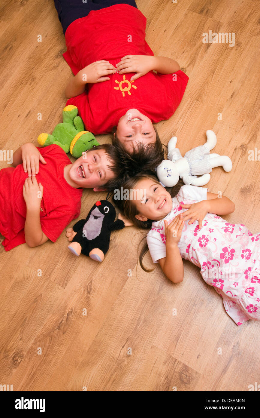 Mädchen, 4 Jahre, und jungen, 6 und 11 Jahren, auf dem Boden liegend, lachen, mit Plüsch-Spielwaren Stockfoto