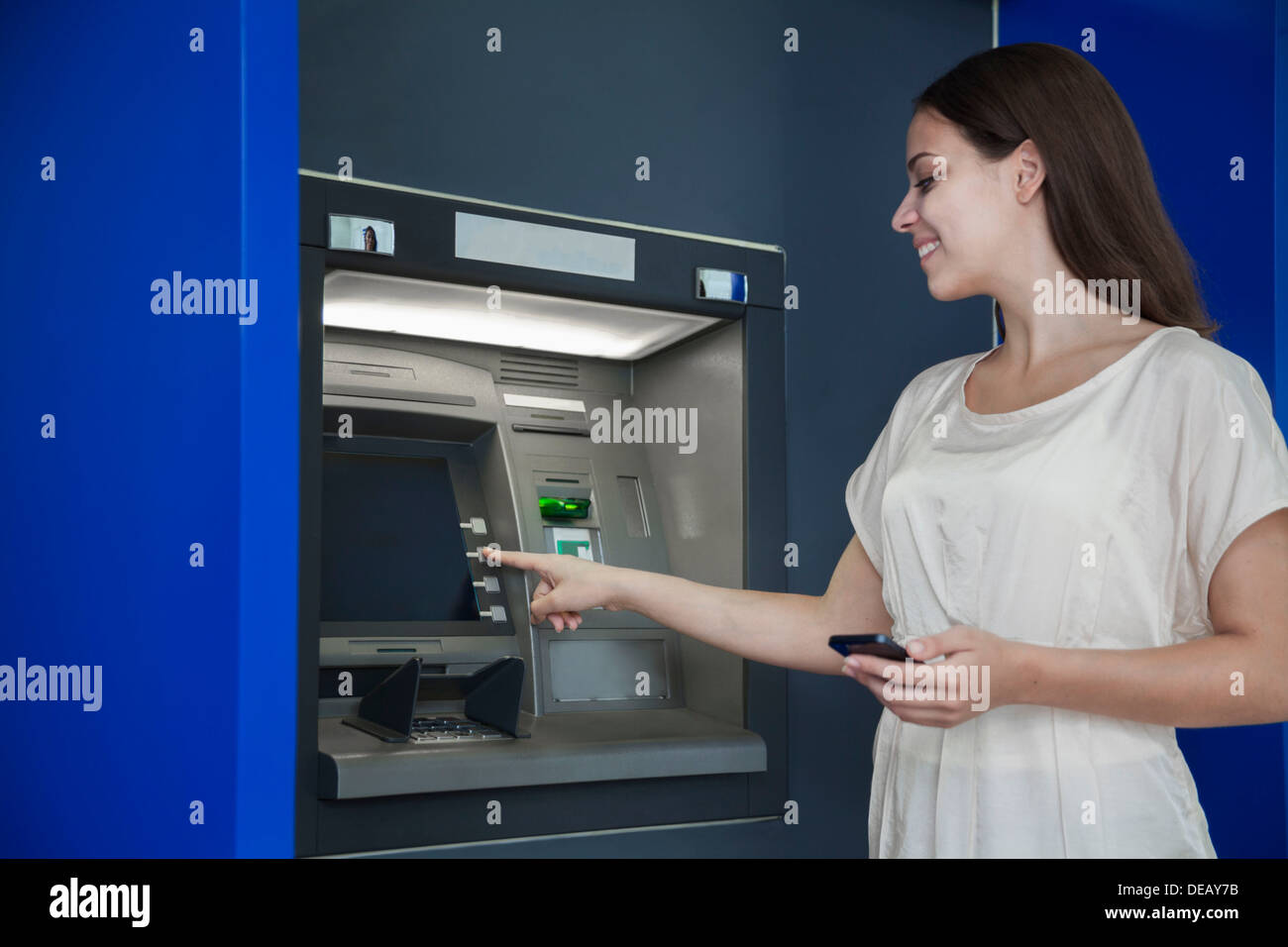 Lächelnde junge Frau, die Geld aus dem Geldautomaten abheben Stockfoto