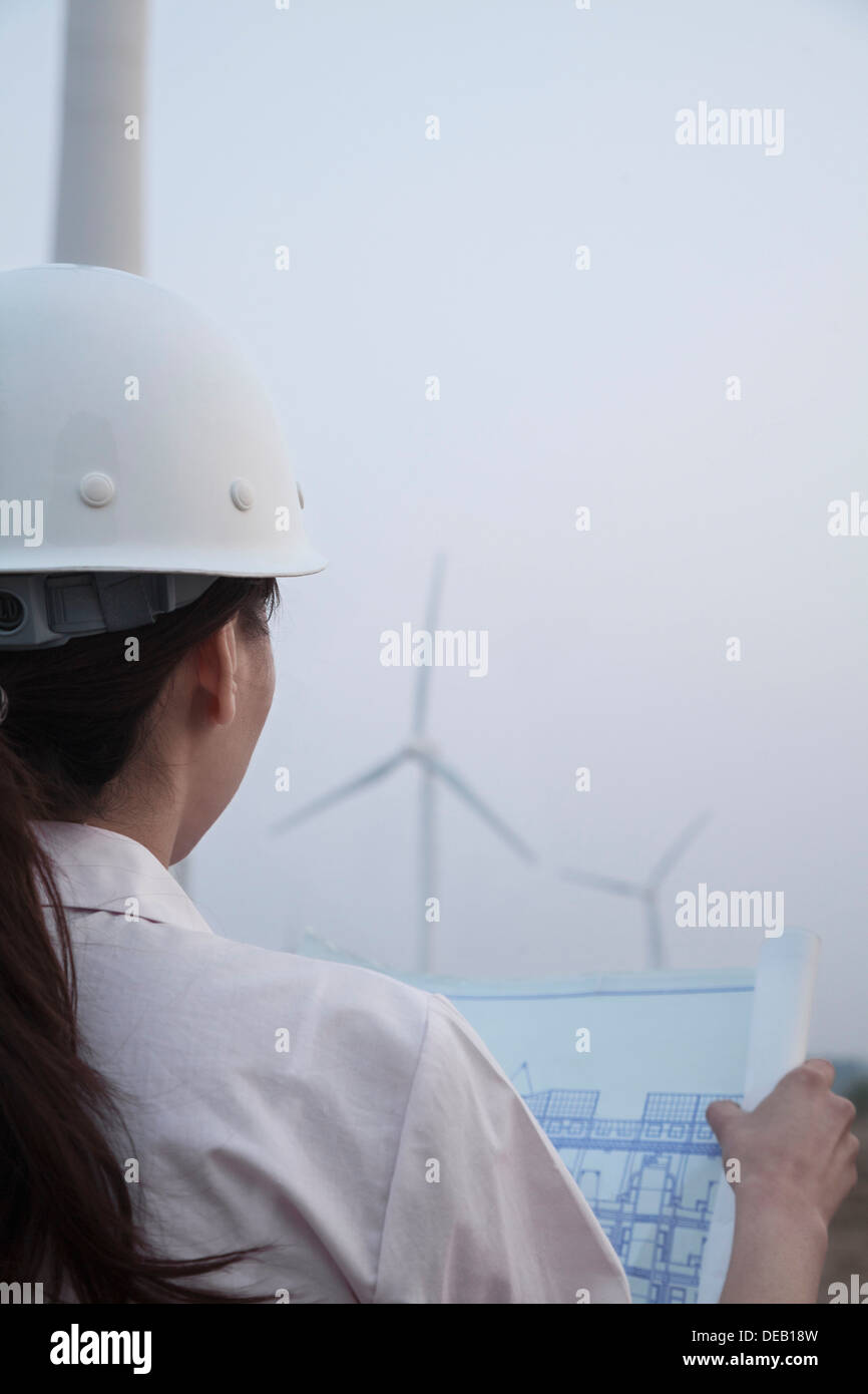 Junge Ingenieurin Blaupause mit Windkraftanlagen vor ihr, über die Schulter-Ansicht betrachten Stockfoto