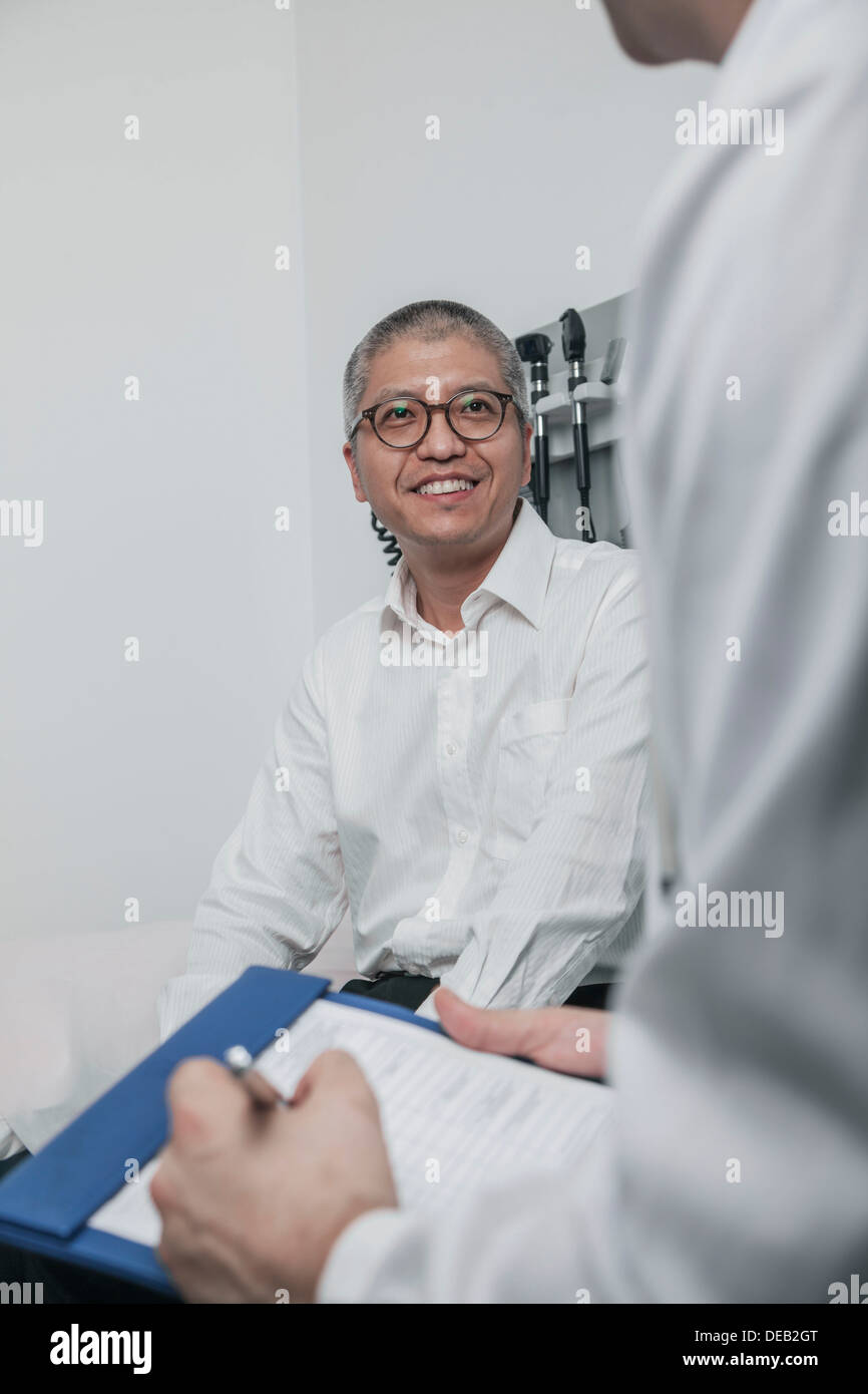 Arzt mit einem Lächeln auf den Lippen Patienten auf medizinische Karte schreiben Stockfoto