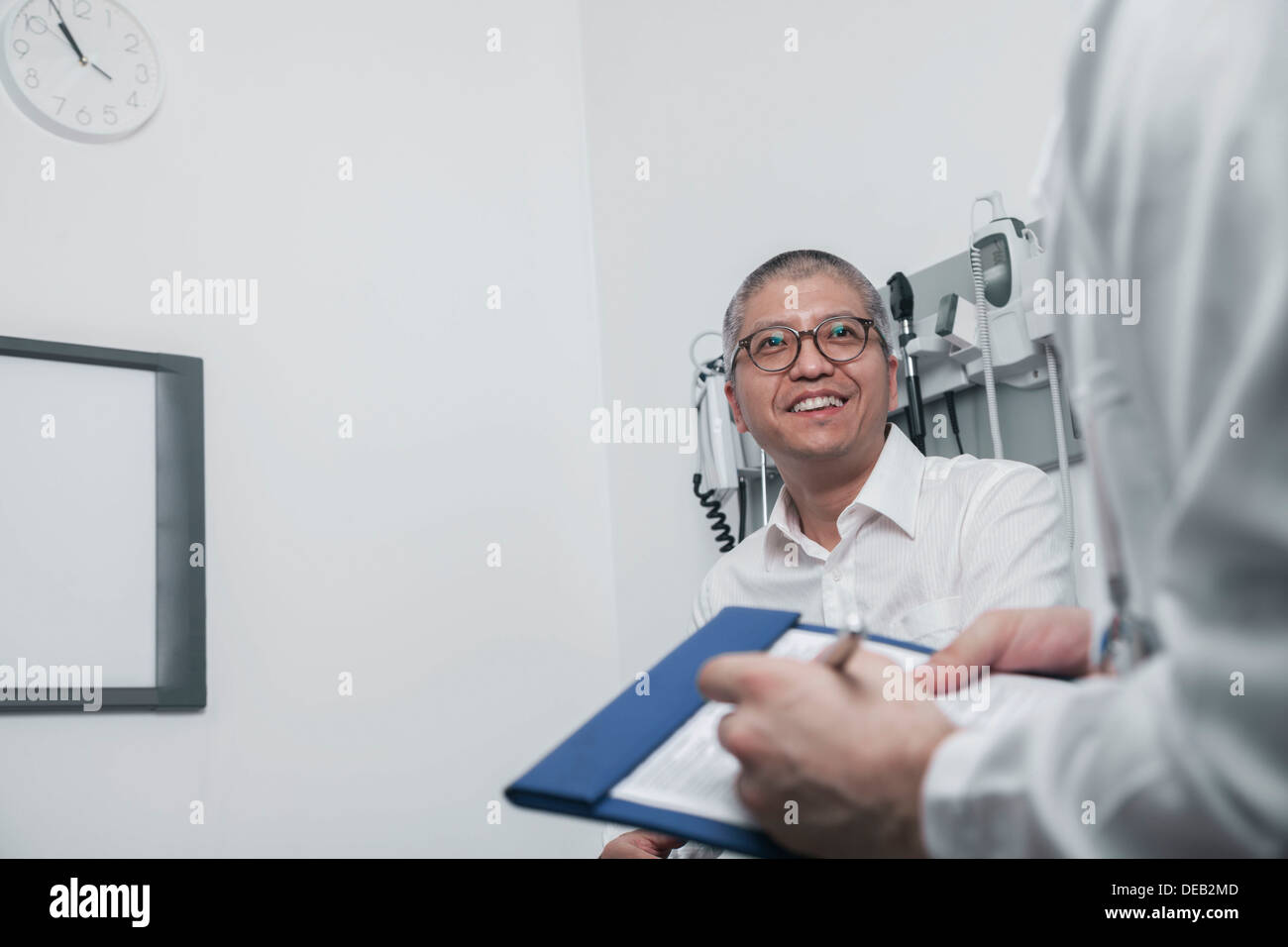 Arzt mit einem Lächeln auf den Lippen Patienten auf medizinische Karte schreiben Stockfoto