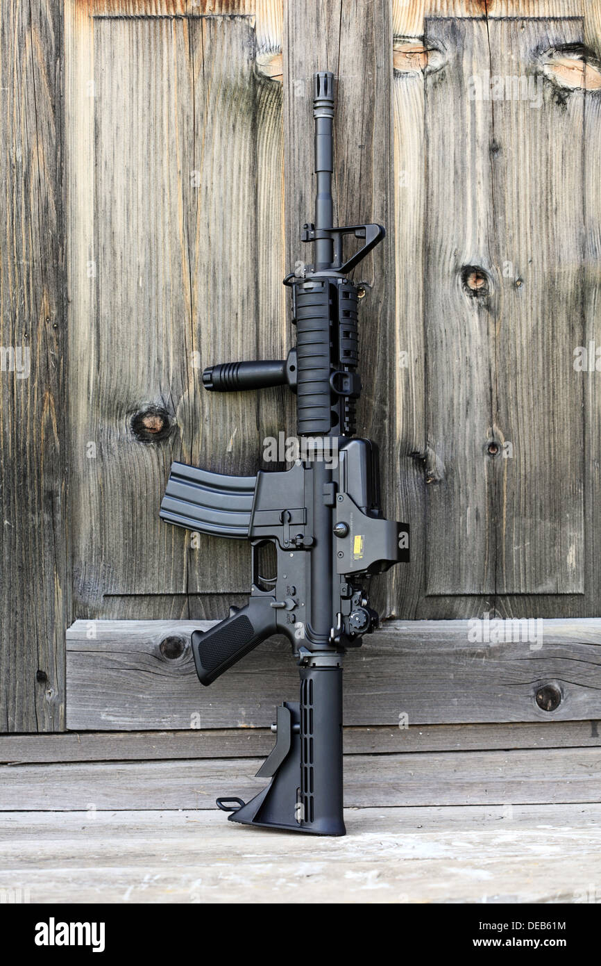 Das schwarze Gewehr. 14,5' AR-15 Carbine (M4A1) mit holographischen Augen gegen eine alte Holztür anzugreifen. Vertikale Zusammensetzung. Stockfoto