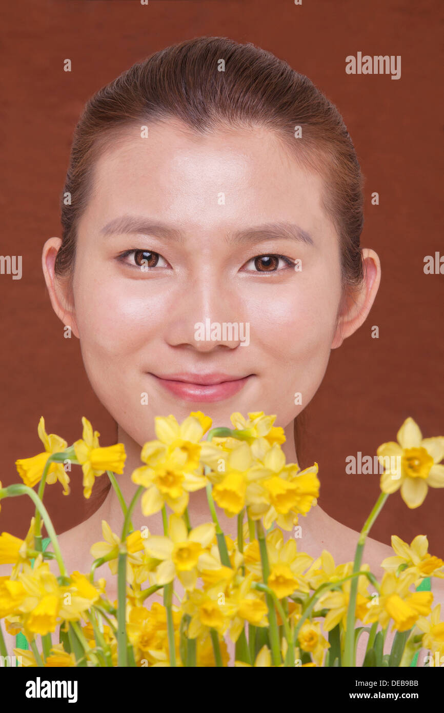 Porträt der lächelnde junge Frau hinter ein paar gelbe Blüten, Studio-Aufnahmen Stockfoto