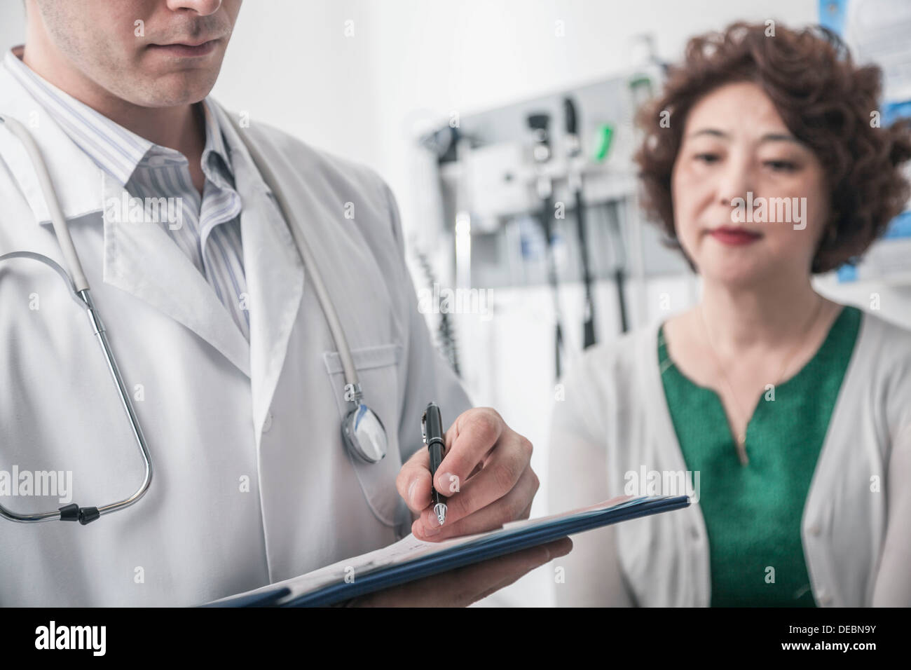 Arzt schriftlich auf medizinischen Diagramm mit Patienten im Hintergrund Stockfoto