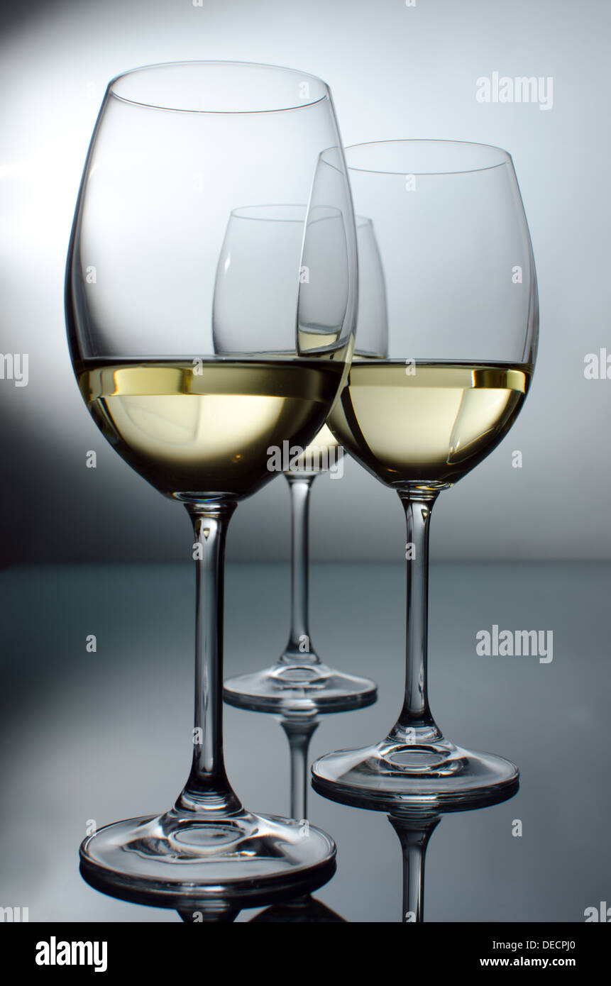 Hintergrundbeleuchtung, drei Gläser Wein auf einem Glastisch Stockfoto