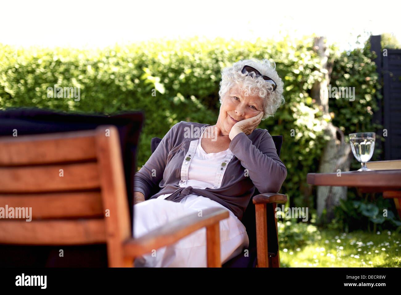 Alte Frau auf Stuhl Blick in die Kamera. Senior weiblich entspannend im Garten genießen ihren Ruhestand Tage Stockfoto