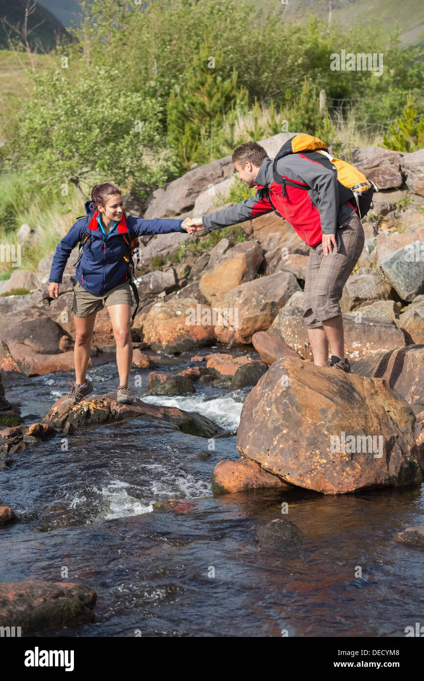 Mann hilft seiner Freundin einen Fluss durchqueren Stockfoto