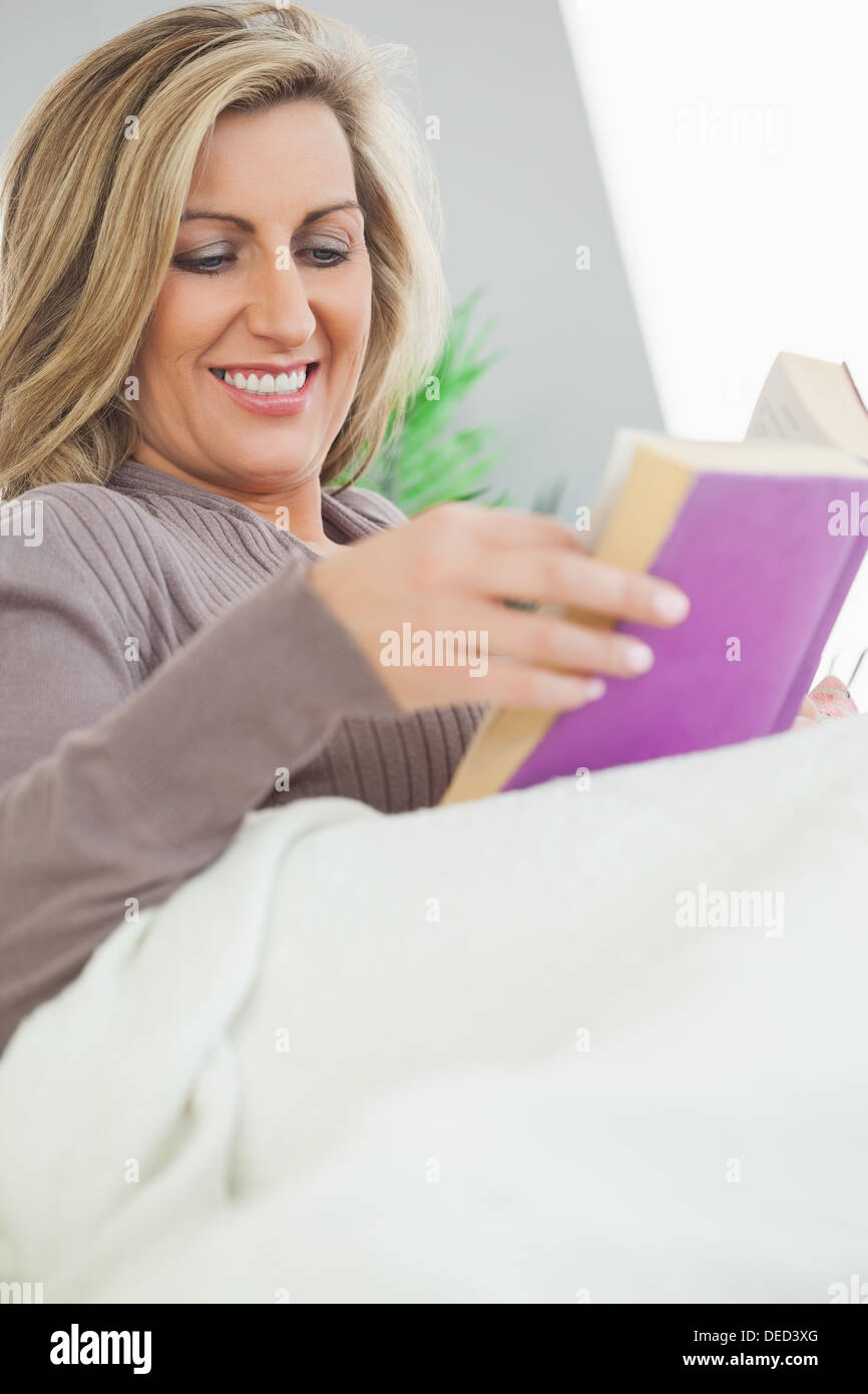 Lächelnde Frau liegend auf dem Sofa ein Buch zu lesen Stockfoto