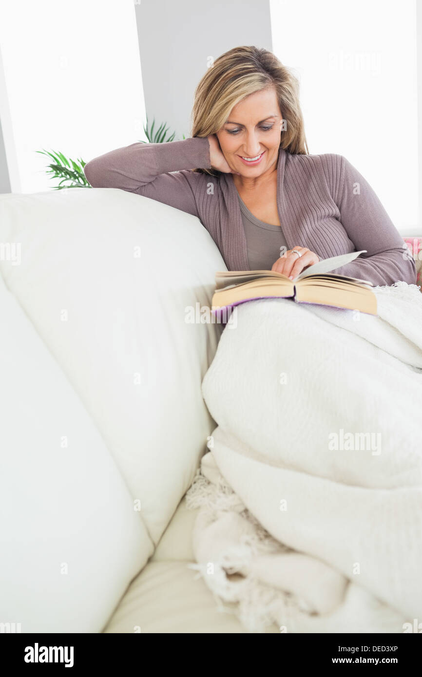 Lächelnde Frau liest ein Buch auf dem sofa Stockfoto
