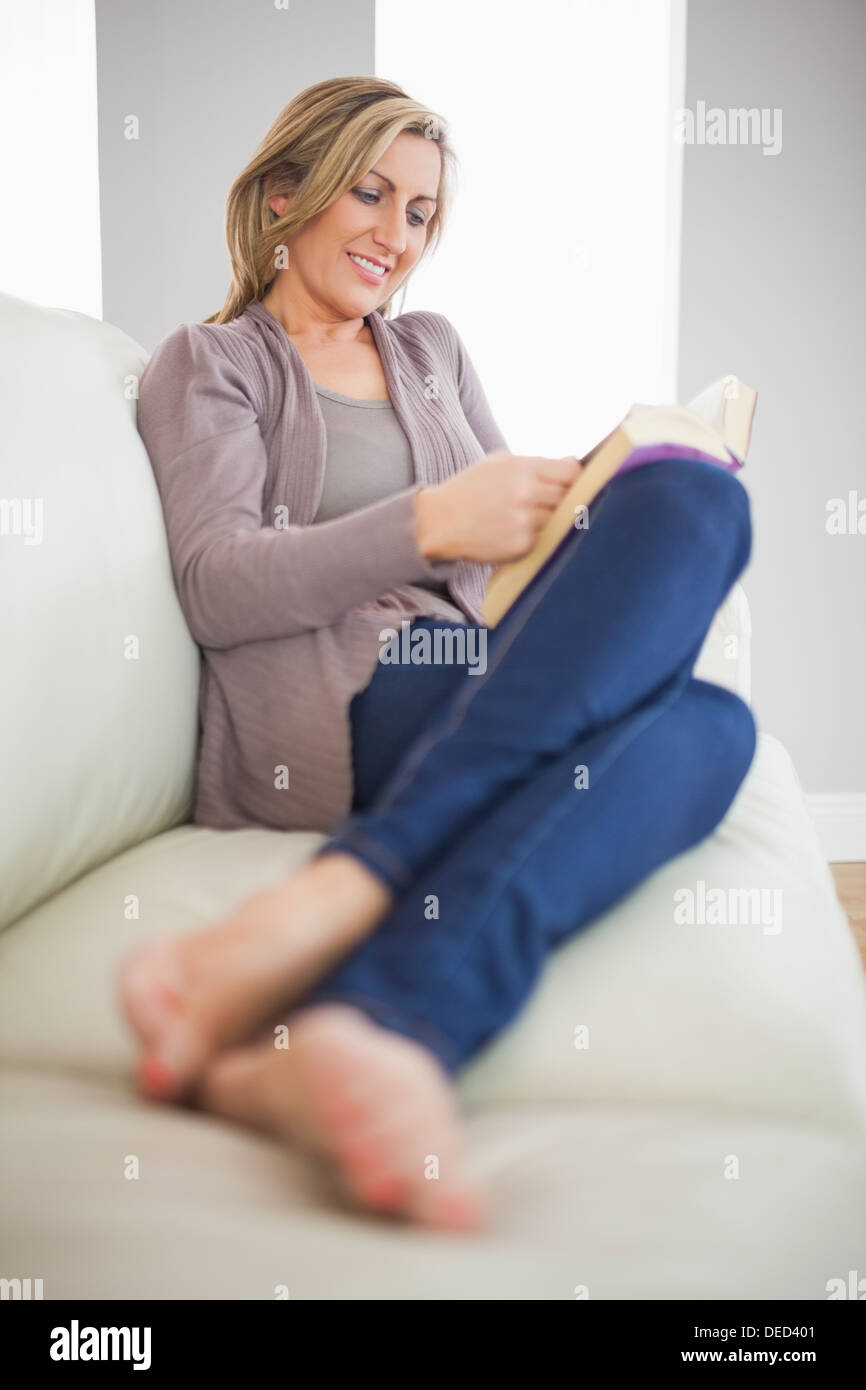 Lächelnde Frau liegend auf dem Sofa ein Buch zu lesen Stockfoto