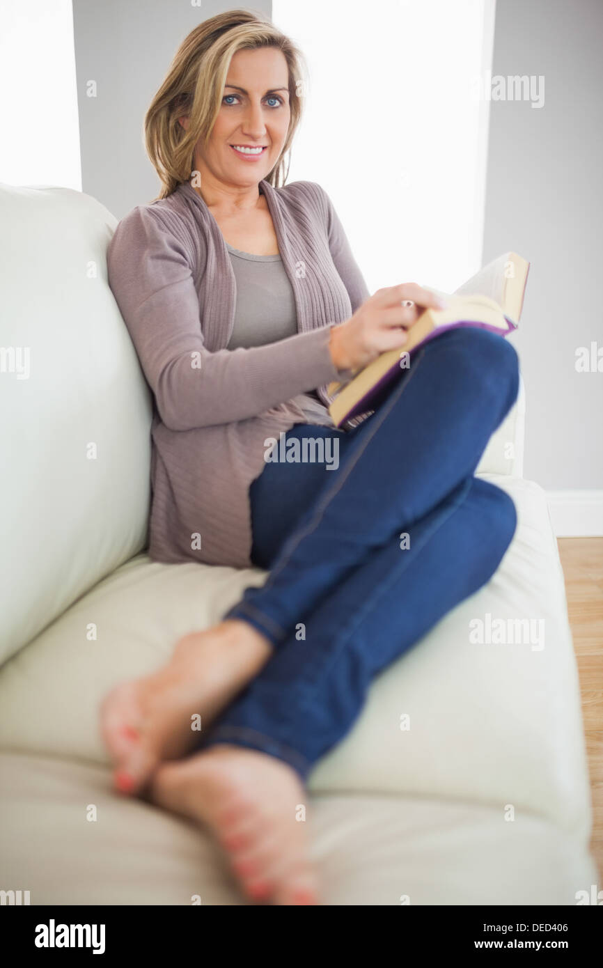 Lächelnde Frau hält ein Buch auf dem Sofa liegend Stockfoto