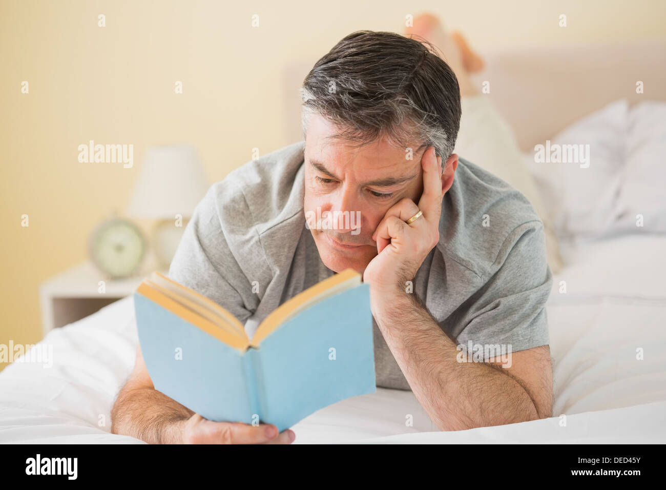 Konzentrierte Mann liest ein Buch auf seinem Bett Stockfoto