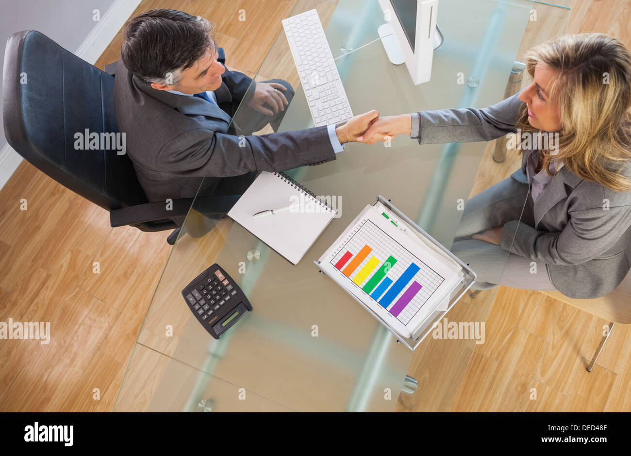 Zwei Geschäftsleute, die mit einem Handschlag über einen Schreibtisch Stockfoto