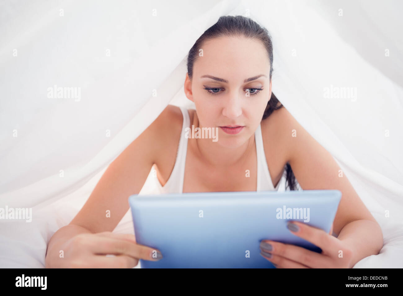 Glücklich Brünette liegen unter der Bettdecke mit ihrem Tablet-pc Stockfoto