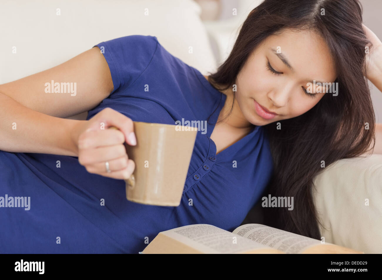 Attraktive asiatische Mädchen lag auf dem Sofa einen Roman lesen und trinken heiße Getränke Stockfoto