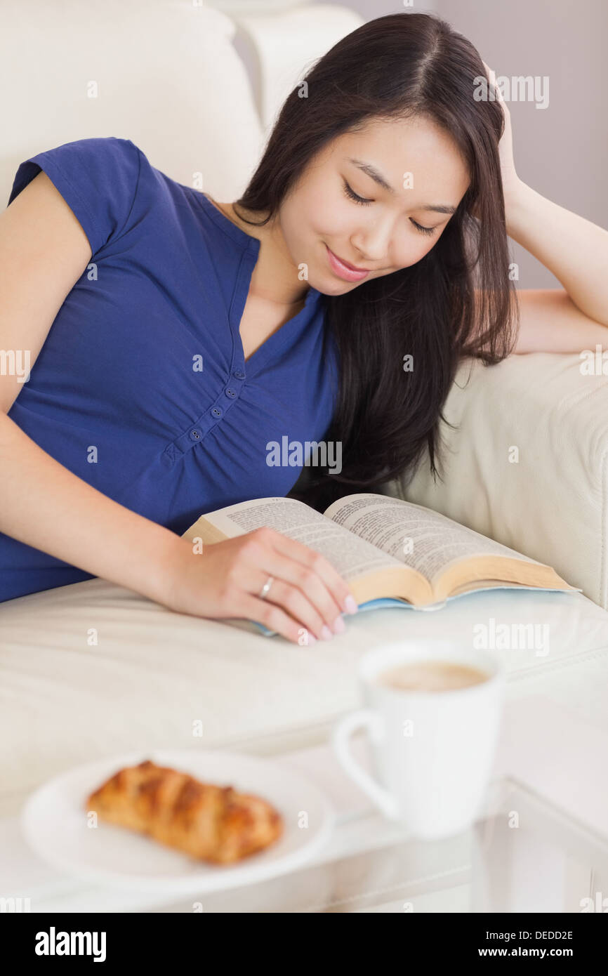 Hübsche junge Asiatin auf dem Sofa ein Buch zu lesen Stockfoto