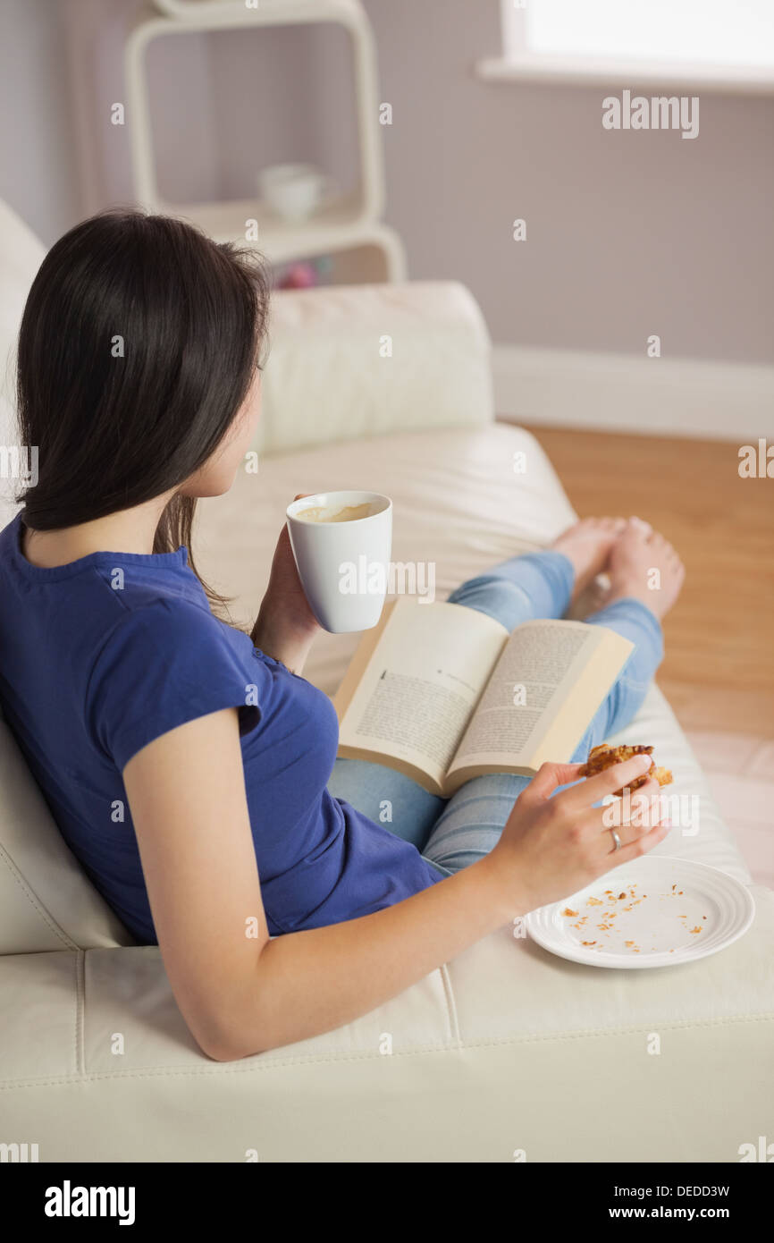 Junge Frau, ein Buch lesen und Essen Gebäck mit Kaffee Stockfoto