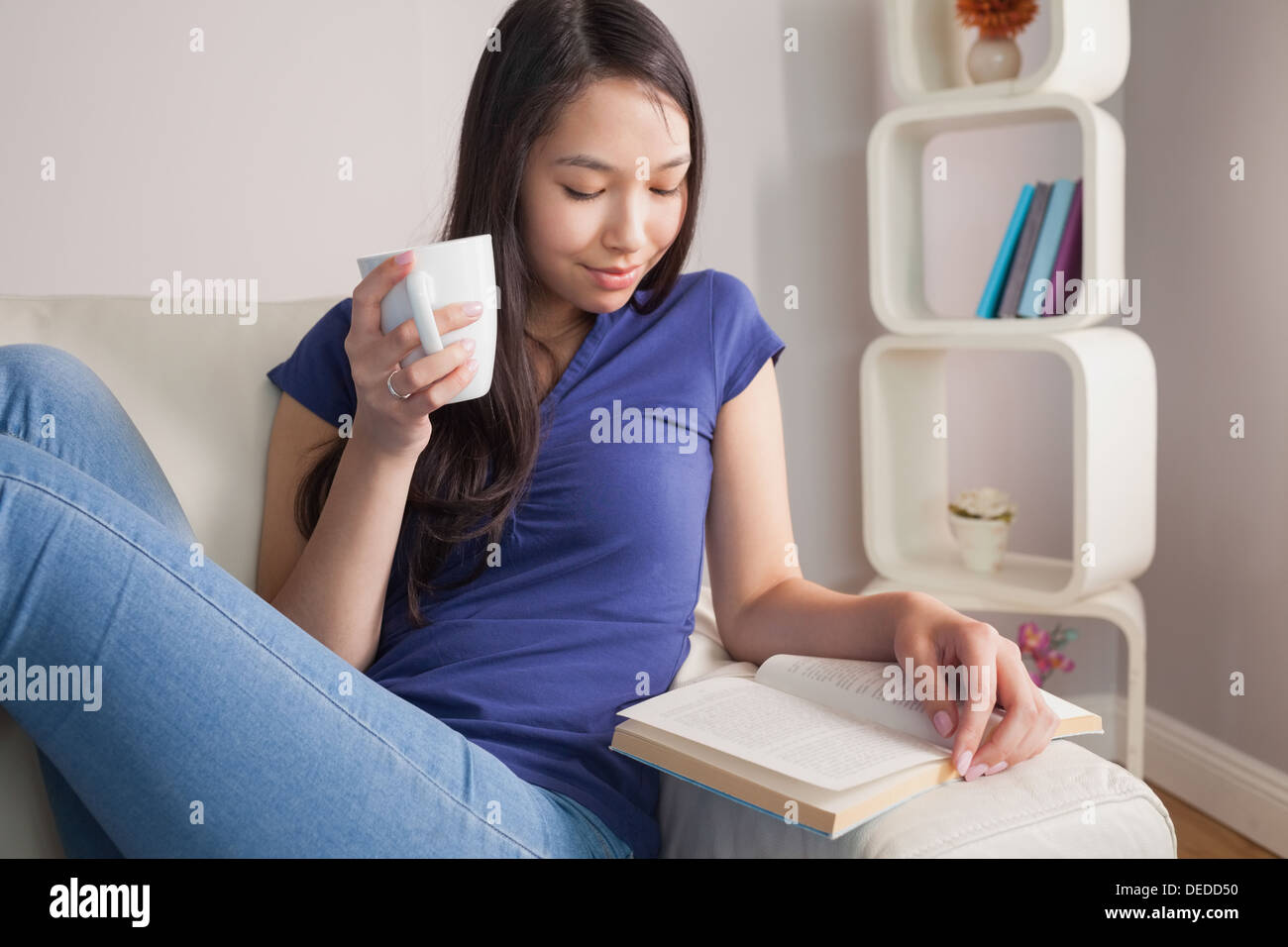 Lesen junge Asiatin auf der Couch halten Becher Stockfoto
