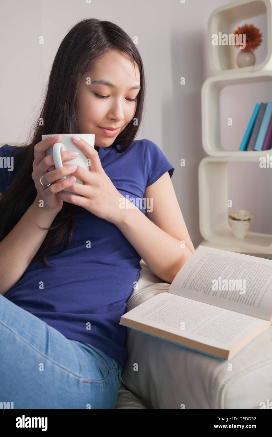 Asiatische Frau sitzen auf der Couch halten Becher lesen Stockfoto