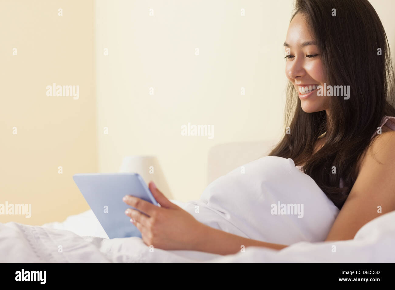 Glückliche junge asiatische Frau sitzen im Bett mit TabletPC Stockfoto