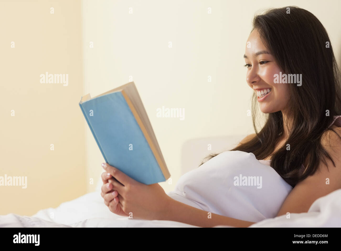Glückliche junge asiatische Frau sitzen im Bett und las ein Buch Stockfoto