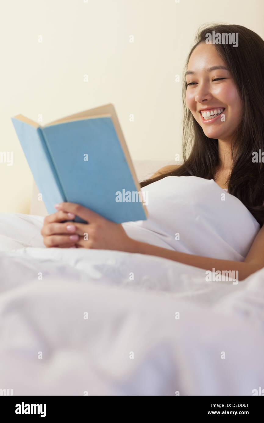Hübsche junge Asiatin, sitzen im Bett und las ein Buch Stockfoto