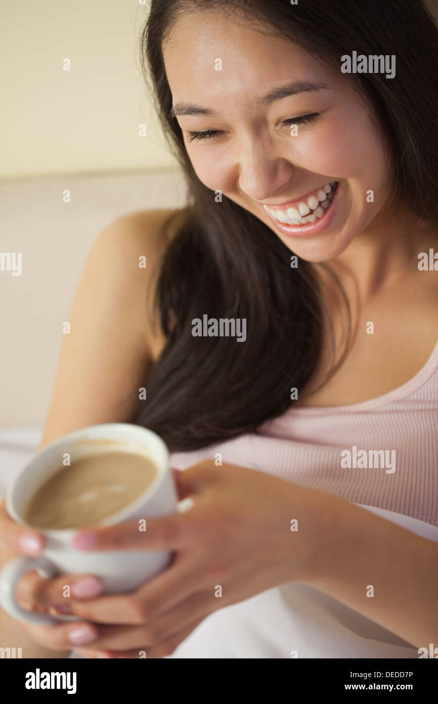 Junge asiatische Frau sitzen im Bett halten ihren Morgenkaffee lachen Stockfoto