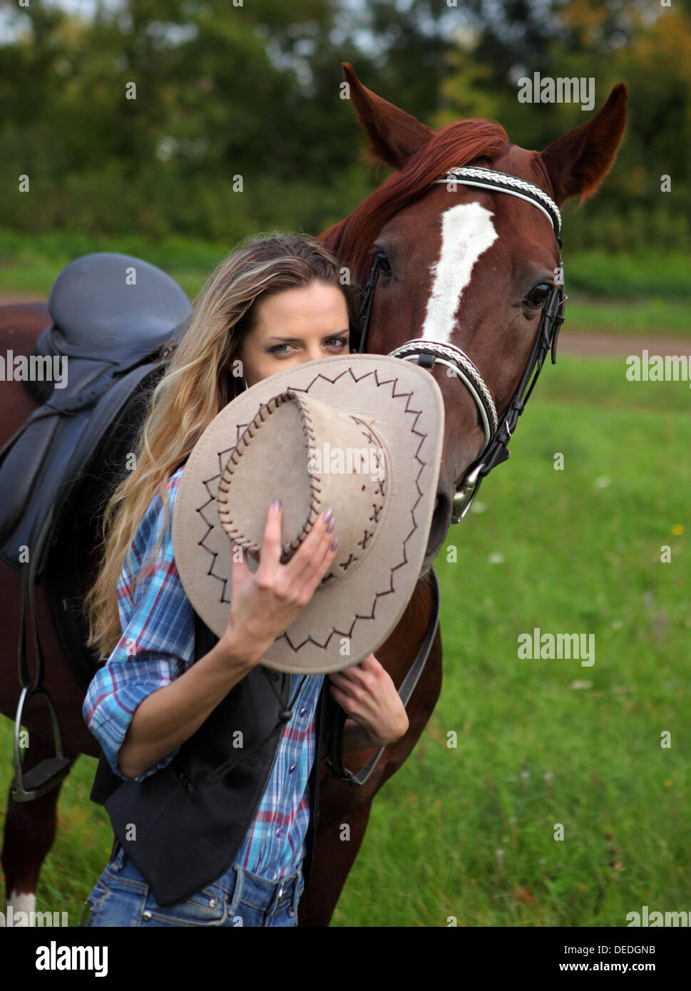 Entzückende junge Frau in einem Cowboy-Hut, ein Pferd durch die Zügel im Freien halten Stockfoto