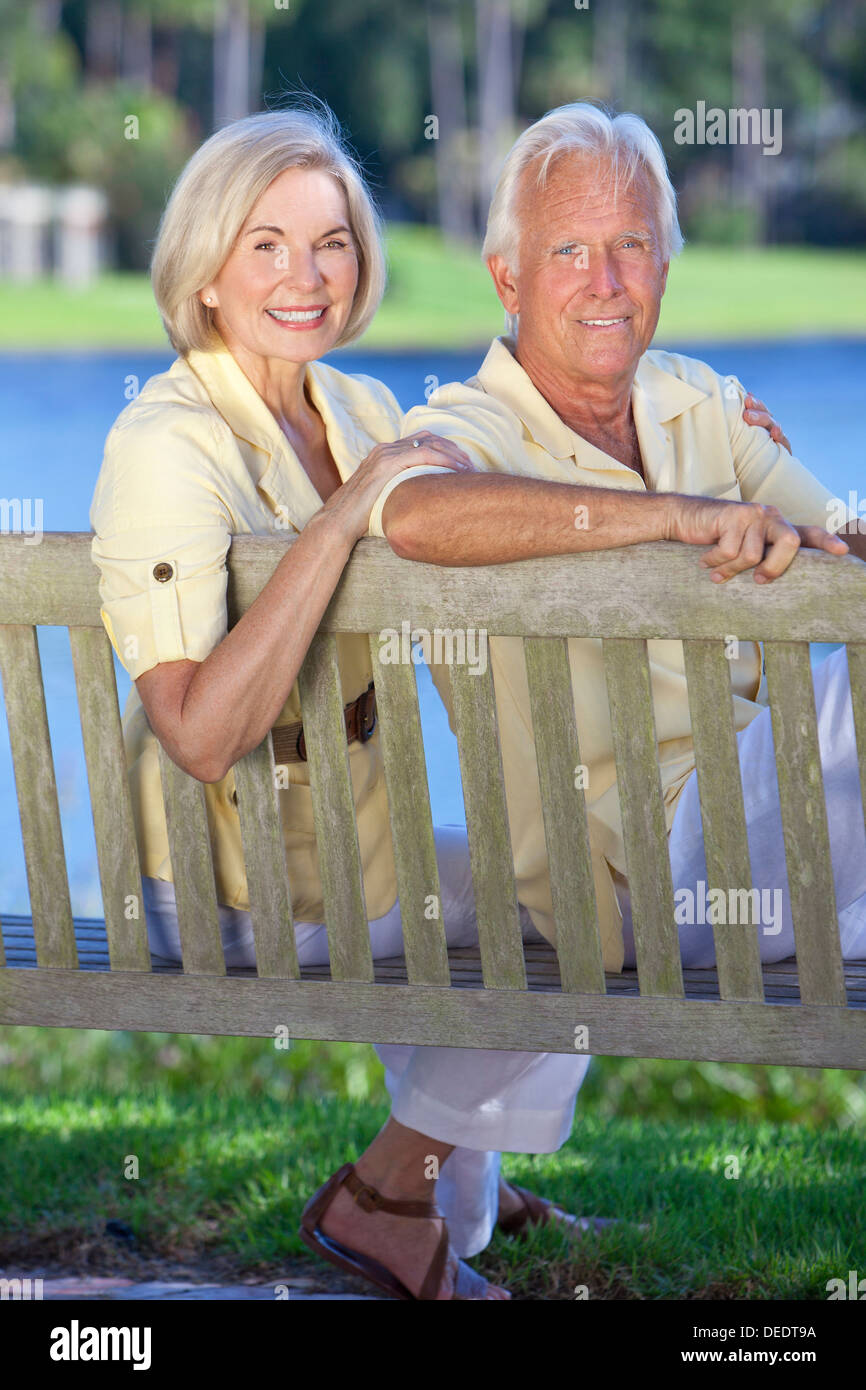 Romantische senior Brautpaar sitzt auf einer Parkbank neben einem blauen See Stockfoto