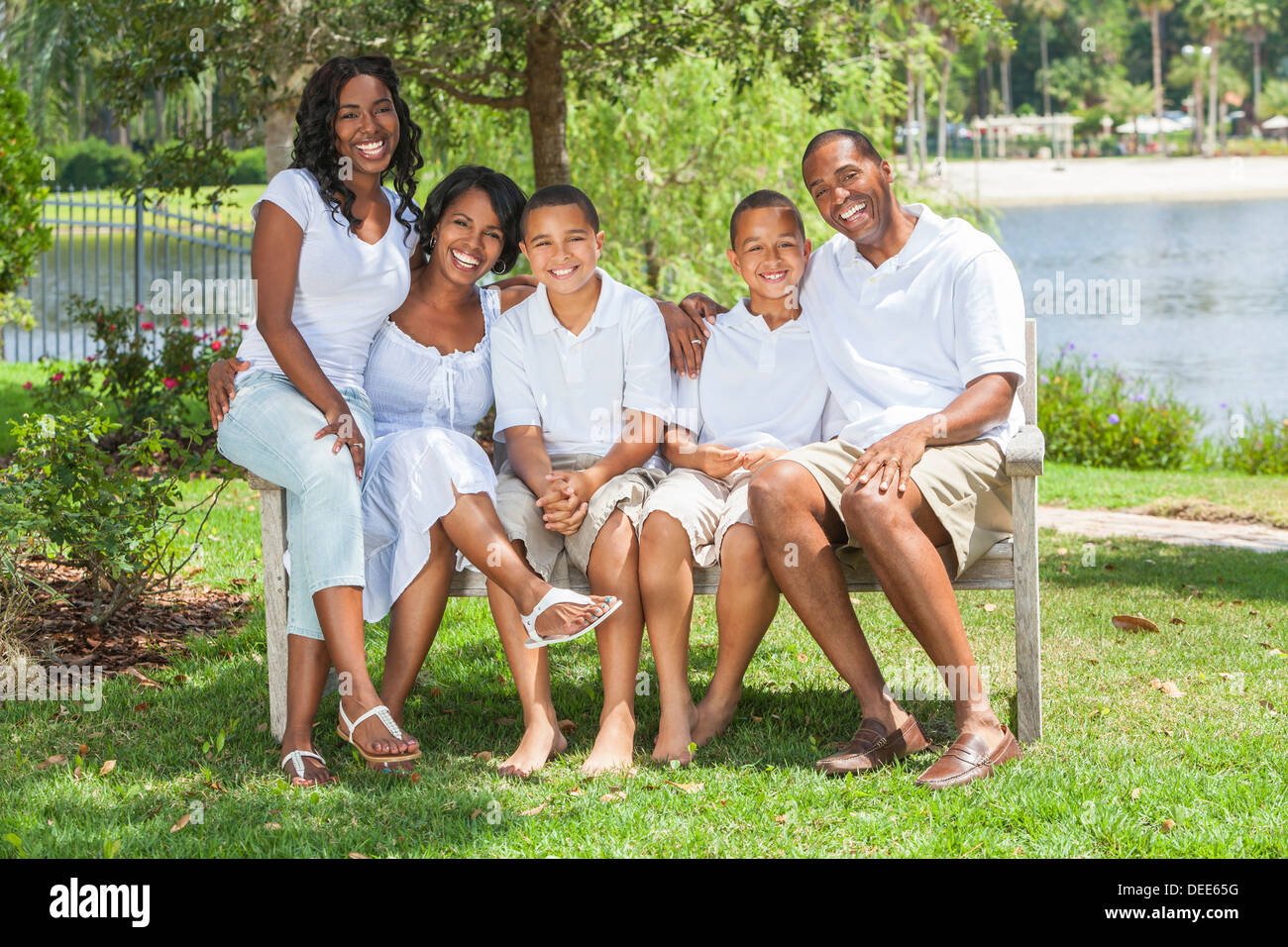 glücklichen schwarzen afroamerikanische Familie zwei Eltern und drei Kinder, zwei jungen ein Mädchen in weißen Kleidern zusammen draußen zu sitzen Stockfoto