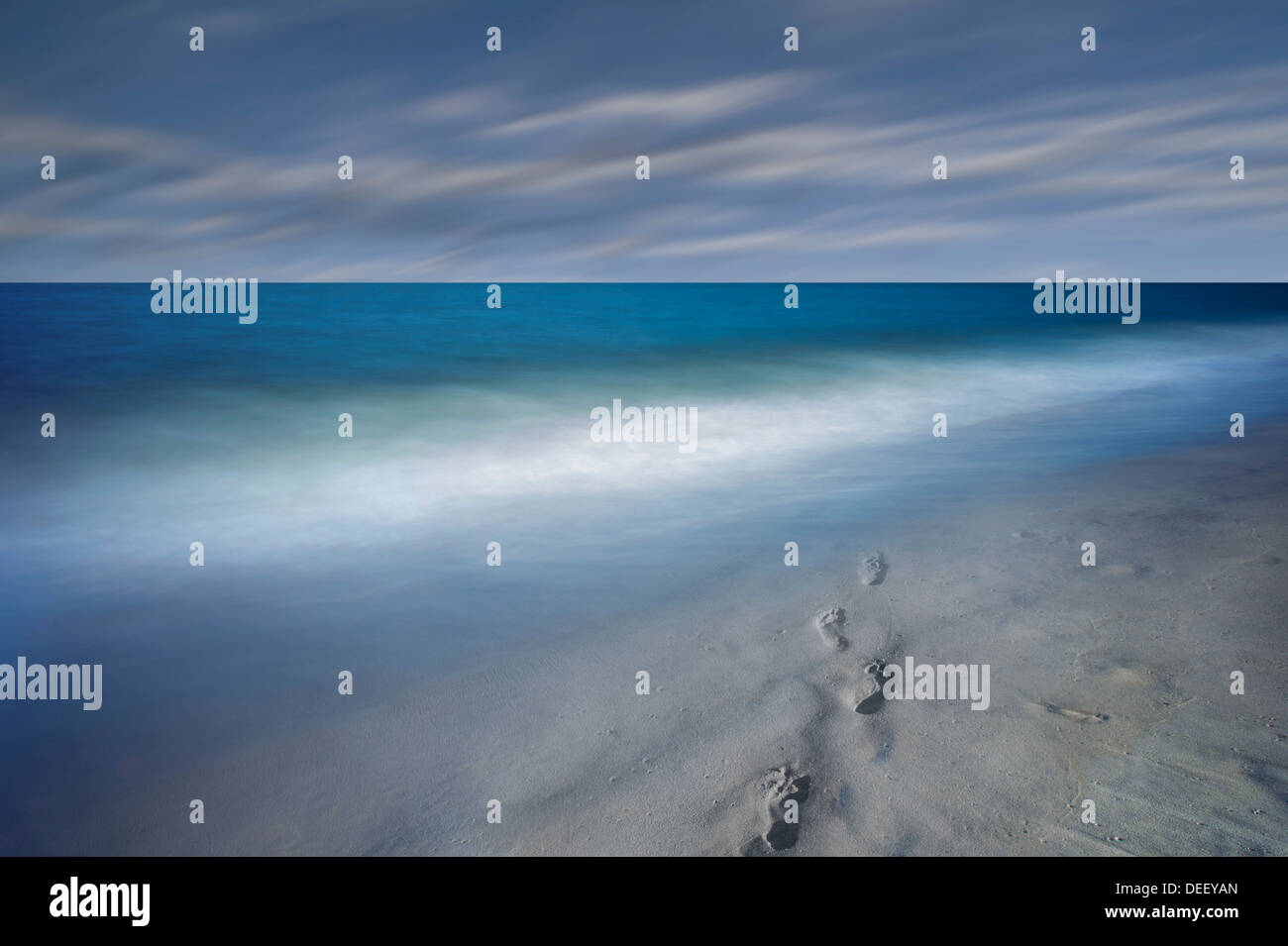 Fußspuren im Sand und verschwommen Meereswellen mit bewegte Wolken Stockfoto